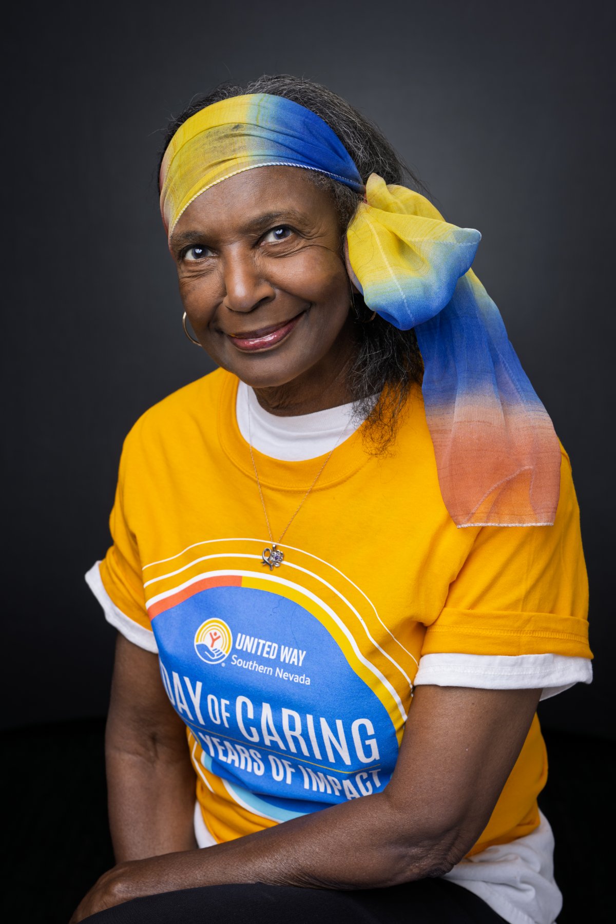 An older adult smiling in a yellow shirt and a blue and gold headscarf